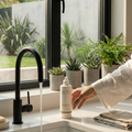 Person washing hands with a bottle of soap in a modern kitchen with plants in the background