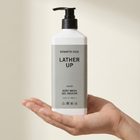 Hand holding a bottle of Kenneth Cole Lather Up body wash against a neutral background
