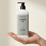 Hand holding a bottle of Kenneth Cole Lather Up body wash against a neutral background