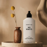 Kenneth Cole 'No Knots' conditioner bottle on a beige surface with a wooden vase and dried flowers.