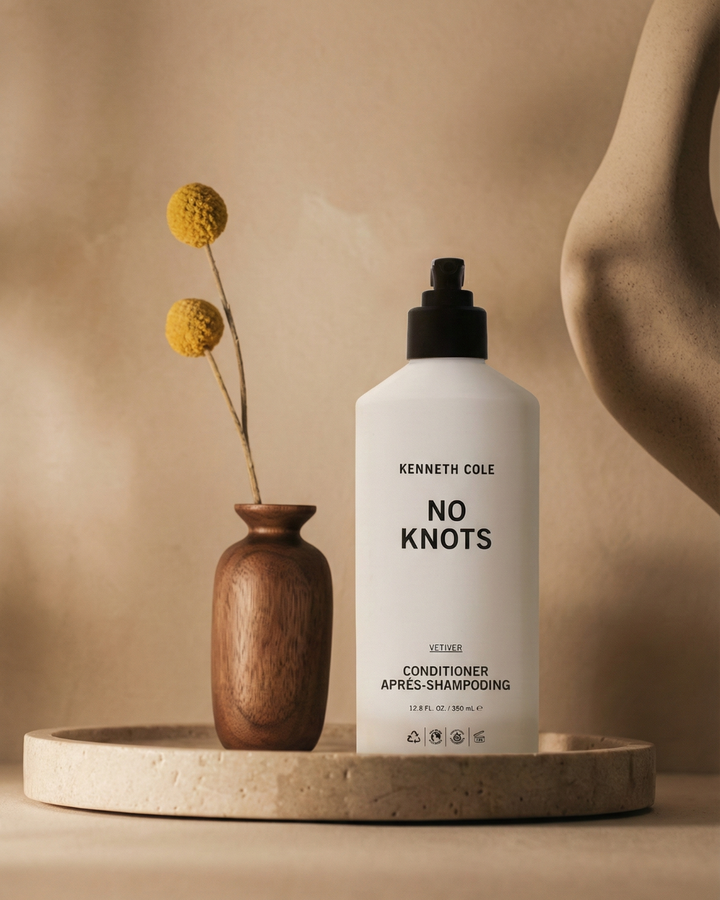 Kenneth Cole 'No Knots' conditioner bottle on a beige surface with a wooden vase and dried flowers.