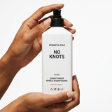 Hand holding a bottle of Kenneth Cole No Knots conditioner against a white background