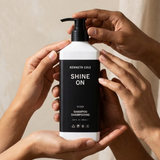 Kenneth Cole Shine On shampoo bottle held by hands against a neutral background