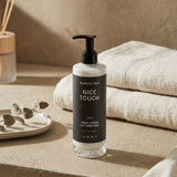 Kenneth Cole Nice Touch body lotion bottle on a neutral background with towels and decor.