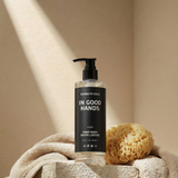 Hand wash bottle labeled 'In Good Hands' by Kenneth Cole on a beige surface with a towel and sponge.
