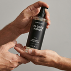 Hand holding a bottle of Kenneth Cole 'In Good Hands' hand wash against a gray background