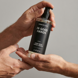 Hand holding a bottle of Kenneth Cole 'In Good Hands' hand wash against a gray background