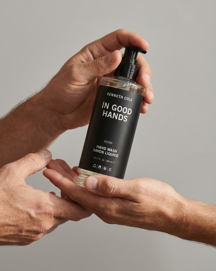 Hand holding a bottle of Kenneth Cole 'In Good Hands' hand wash against a gray background