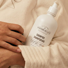 Person holding a bottle of Woodbury & Co shampoo with a neutral background