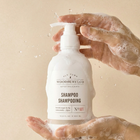 Bottle of Woodbury & Co. shampoo held by hands with soap suds on a beige background