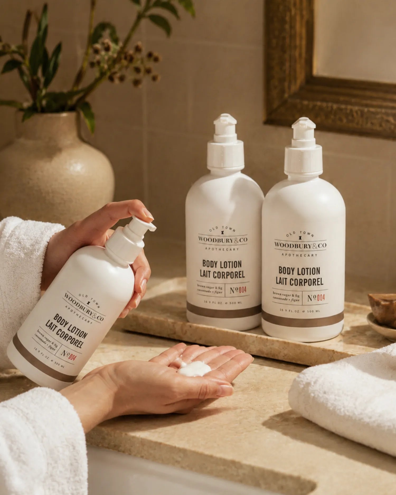 Guest dispensing Woodbury & Co body lotion beside folded towels on a stone hotel bathroom counter